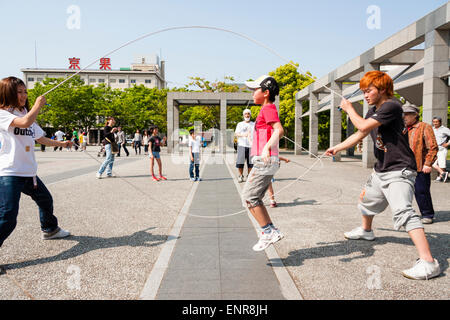 Seitenansicht eines jungen japanischen Jungen springen in springen Wettbewerb mit Mädchen hält Ende von zwei Springseile und orange behaart Junge hält andere Enden. Stockfoto