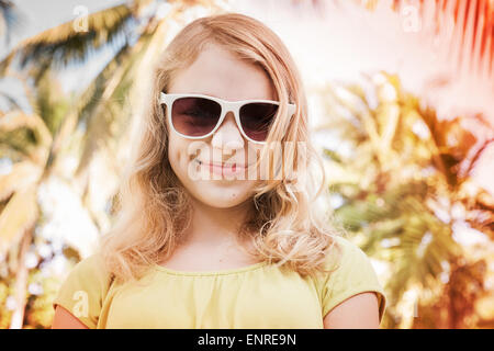 Blonde lächelnde Teenager-Mädchen in Sonnenbrillen, getönten Nahaufnahme outdoor Sommer Portrait mit Palmen auf einem bunten Hintergrund Foto mit Stockfoto