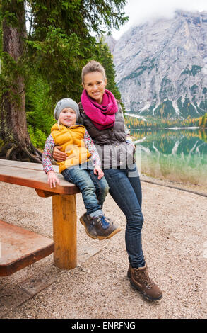 Eine Mutter lehnt sich auf dem hölzernen Picknicktisch, die ihre Tochter sitzt. Sie ruhen. Gekleidet in Outdoor-Ausrüstung und Wanderschuhe Stockfoto