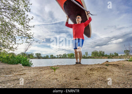 Senior männlichen Paddler tragen seine SUP Paddleboard am Ufer eines Sees in Colorado, Vorfrühling Stockfoto