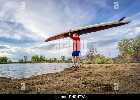 Senior männlichen Paddler tragen seine SUP Paddleboard am Ufer eines Sees in Colorado, Vorfrühling Stockfoto