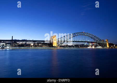 Ein Boot fährt vorbei an der Sydney Harbour Bridge bei Nacht gegen den blauen Himmel. Stockfoto