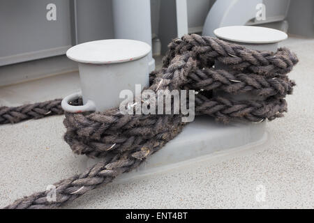 Nahaufnahme von einem Liegeplatz Seil mit einem verknotete Ende um eine Klampe auf einem hölzernen Pier gebunden / nautische mooring Seil Stockfoto