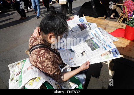 Ältere chinesische Frau liest chinesische Zeitung im Freien. Wirtschaft in China. Stockfoto