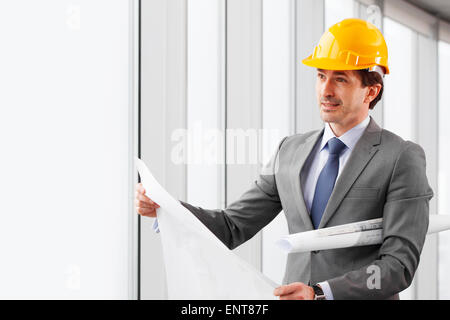 Geschäftsmann in Arbeitshelm mit Blaupausen Stockfoto