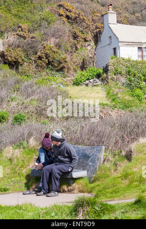 Junges Paar, das im Mai auf der Bank im Trefin oder Trevine im Pembrokeshire Coast National Park, Wales, Großbritannien sitzt Stockfoto