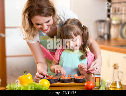 Süße Mutter mit Kind Tochter bereitet Fisch in Küche Stockfoto