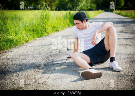 Hübscher junger Mann Ruhe sitzen auf der Straße nach laufen und Joggen im Land an einem sonnigen Tag Stockfoto