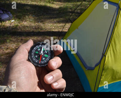 Kompass und touristische Zelt. Die magnetischen Kompass in der Hand gegen das Zelt im Wald im Frühjahr. Stockfoto