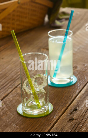Zwei Getränke Gläser auf einem Picknick-Tisch, ein Glas gefüllt mit Limonade und Picknick-Korb im Hintergrund. Stockfoto
