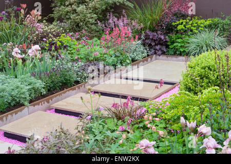 Moderner Garten schwimmende Trittsteinpflaster über rosa Kies mit gemischten krautigen Blumenränder - Frühling - England UK - RHS Malvern Frühjahrsshow Stockfoto