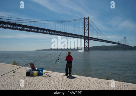 Die Tejo-Fluss-Brücke oder 25. April Brücke (Ponte 25 de Abril) mit einem Fischer am Ufer des Flusses in Lissabon, Portugal Stockfoto