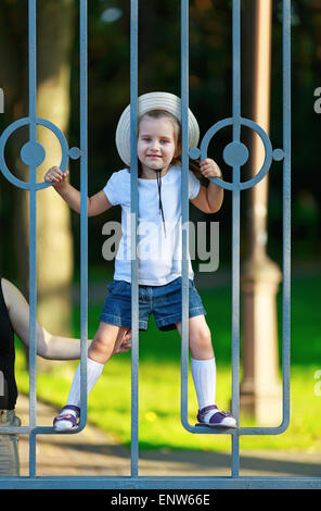 Glückliches Kind klettert auf den Bars von einem Metallzaun. Warmen, sonnigen Sommertag. Vertikale erschossen. Stockfoto