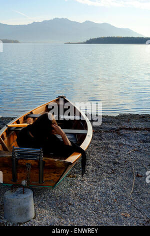 Frau sitzt in einem Schlauchboot auf Stein Strand mit Blick auf den See zu den Bayerischen Alpen, Chiemsee, Chiemgau, obere Bayern Deutschland Europa Stockfoto