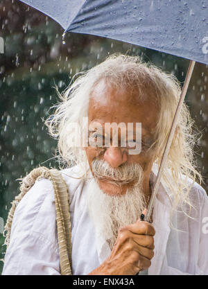 Sadhu hält einen Regenschirm im Regen an der Sri Ramana Ashram in Tiruvannamalai, Indien Stockfoto