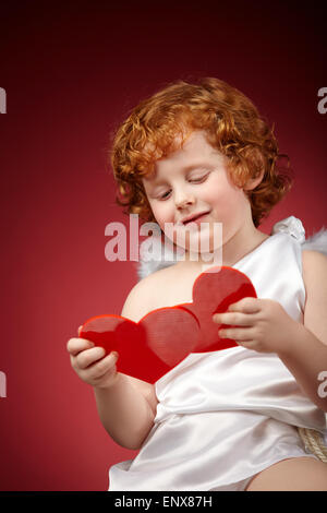 Kleiner Junge mit Flügeln hinter dem Rücken hält zwei Herzen Stockfoto