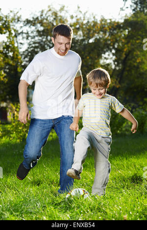 Fröhliche Vater und Sohn aufholen mit einem Fußball im park Stockfoto