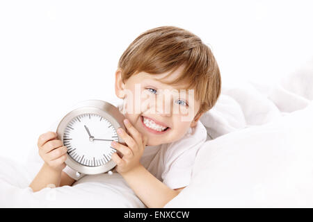 Der lächelnde junge liegt im Bett mit einem Wecker in Händen Stockfoto