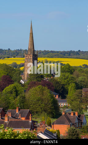 St. Johannes Kirche dominiert die Landschaft in der kleinen Stadt Bromsgrove in Worcestershire mit Feldern von Raps hinter Stockfoto