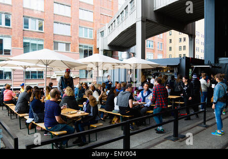 USA, New York, Manhattan, Menschen, die an den Tischen unter Sonnenschirmen an einem Essen Ort am Chelsea Markt Übergang auf die lineare High Line Park auf einem stillgelegten erhöhte Eisenbahn Sporn die West Side-Linie genannt. Stockfoto