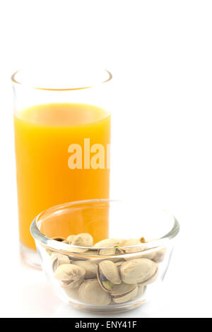 Pistazien in einer Glasplatte und Glas Orangensaft isoliert auf weiss Stockfoto