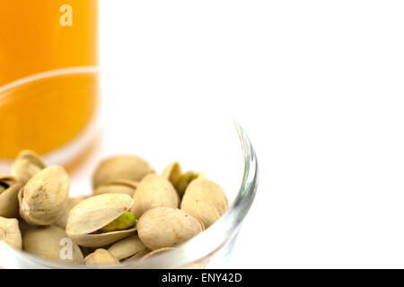 Pistazien in einer Glasplatte und Glas Orangensaft isoliert auf weiss Stockfoto