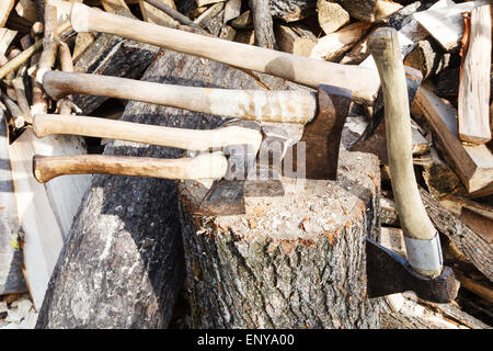 viele verschiedene Achsen in Holzklotz in der Nähe von Haufen von Brennhölzer Stockfoto