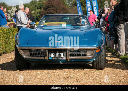 Front-End-Blick auf eine blaue, klassische amerikanische Korvette Sportwagen auf einem Kiesweg mit Fahrer und mehrere auf Zuschauer in der Nähe. Stockfoto