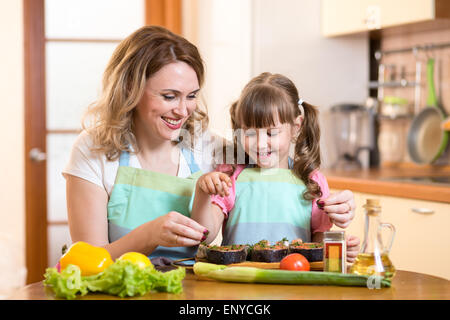 Nette Frau mit Kind Tochter bereitet Fisch in Küche Stockfoto