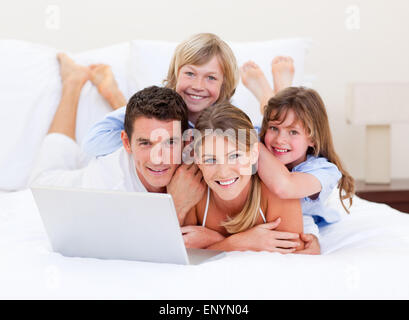 Lächeln, Familie mit Blick auf einen Laptop auf dem Bett liegend Stockfoto