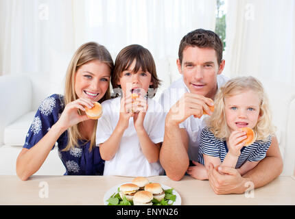 Begeisterte Familie essen Burger im Wohnzimmer Stockfoto