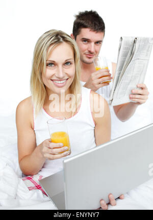 Paar Orangensaft trinken und Lesen von Nachrichten im Bett Stockfoto