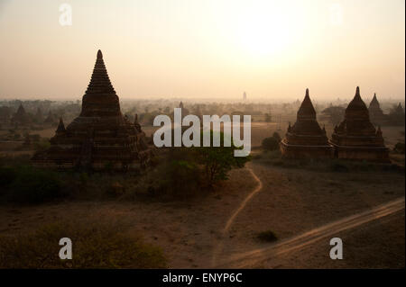 Ein einsamer Tourist sitzt oben auf dem dunklen Silhouetten der Tempel gegen den gelb leuchtenden Himmel bei Sonnenaufgang Bagan Myanmar Stockfoto