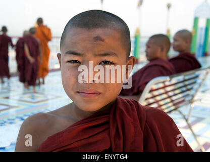 Ein buddhistischer Novize schaut die Kamera mit fünf Mönch im Hintergrund in einem Sagaing-Tempel in der Nähe von Mandalay Myanmar Stockfoto