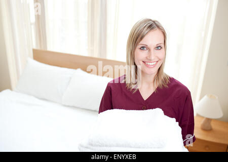 Strahlende Putzfrau hält Handtücher in einem Hotelzimmer Stockfoto