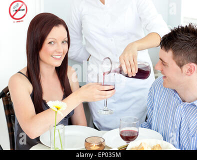 Fröhliche junge Paar beim Abendessen im Restaurant mit Kellner serviert ihnen Wein Stockfoto