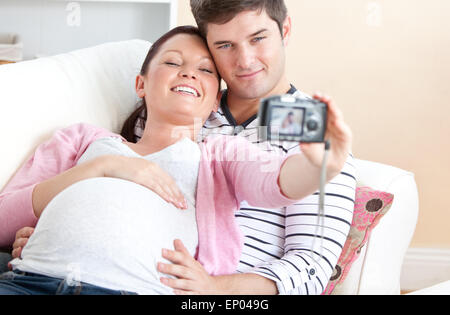 Eine fröhliche schwangere Frau und ihr Mann die Bilder von sich selbst auf einem Sofa in Nahaufnahme Stockfoto