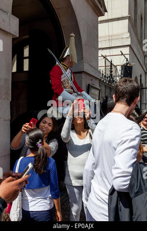 Touristen nehmen Selfies von sich selbst und einer berittenen Gardisten am Eingang zu Horseguards Parade, Whitehall, London, England Stockfoto