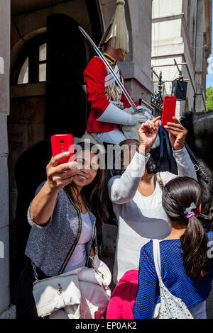 Touristen nehmen Selfies von sich selbst und einer berittenen Gardisten am Eingang zu Horseguards Parade, Whitehall, London, England Stockfoto
