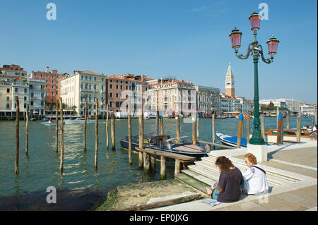 Venedig, Italien - 24. April 2013: Leute sitzen neben dem Canal gegen einen Überblick über klassische venezianische Architektur. Stockfoto