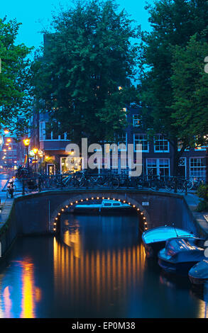 Abenddämmerung in Amsterdams Altstadt mit einer Brücke und Licht spiegelt sich im Kanal. Stockfoto