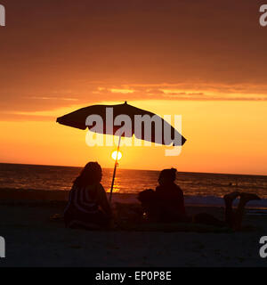 Menschen sitzen und liegen unter dem Sonnenschirm am Sandstrand Cavancha bei Sonnenuntergang in Iquique, Chile Stockfoto