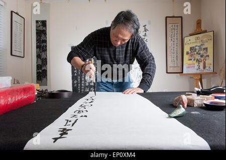Asiatischer Mann mit einem Pinsel, um Kalligraphie auf ein großes weißes Blatt Papier in Gaithersburg, Maryland zu malen. Stockfoto