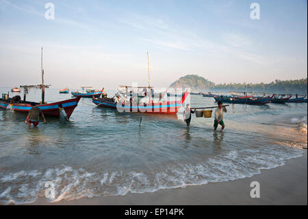 Zwei Fischer entladen Sie Körbe mit Fischen aus ihrer Fischerboot vor Anker am Ngapali Strand am frühen Morgen Myanmar Stockfoto