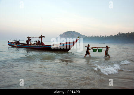 Zwei Fischer entladen Sie Körbe Fisch aus ihrer Fischerboot vor Anker am Ngapali Strand im Morgengrauen Myanmar Stockfoto