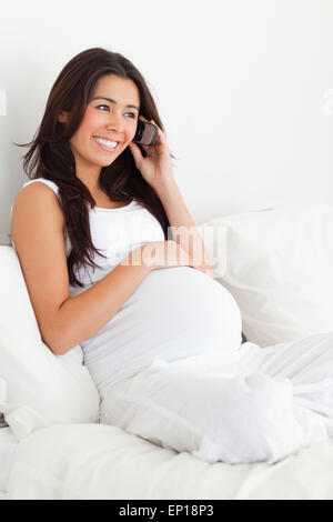 Gut aussehende schwangere Frau am Telefon auf einem Bett liegend Stockfoto