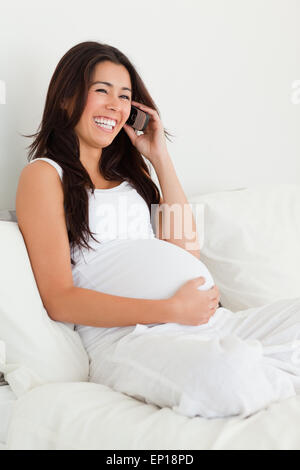 Schöne schwangere Frau am Telefon auf einem Bett liegend Stockfoto