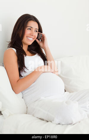 Attraktive schwangere Frau am Telefon auf einem Bett liegend Stockfoto