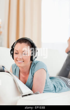 Attraktive Frau mit Kopfhörern eine Zeitschrift liest, während auf einem Sofa liegend Stockfoto