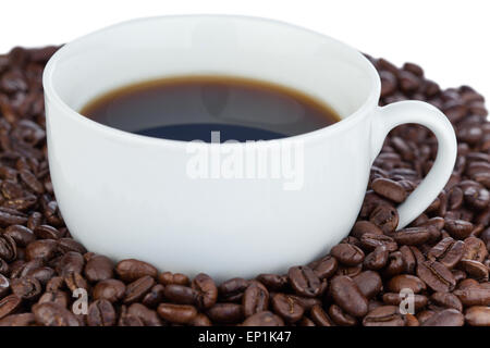 Weiße Tasse Kaffee umgeben mit Kaffeebohnen Stockfoto